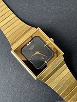 Close-up of the watch face showing the rectangular black dial, gold-tone hands and markers, and decorative stones at 12 o'clock.