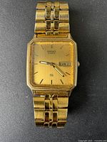 Front view of vintage Seiko watch showing gold-tone rectangular dial with day and date display at 3 o'clock. Light scratches on face and case visible.