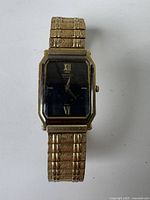 Full front view of vintage Seiko men's watch showing black rectangular dial with gold Roman numerals and gold-tone textured metal bracelet.