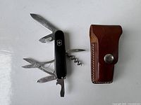 Vintage Swiss Army pocket knife with tools opened displayed next to a brown leather belt case.