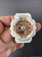 Close-up of front dial of Casio Baby-G watch showing white resin case and band, rose gold dial accents, and control buttons labeled Adjust, Mode, Light, Search. The watch shows use wear and dirt.