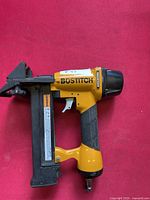 Side view of the Bostitch pneumatic air fastener tool showing yellow magnesium body and black handle with air fitting at the base.