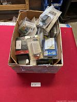 Box of various packaged electrical items including switches, timers, and controls on a red surface.