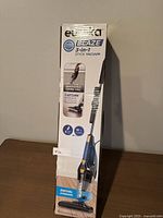 Front of sealed box showing Eureka Blaze 3-in-1 stick vacuum with features like removable hand vac, 3 speed fan, 18 ft cord, and swivel steering.