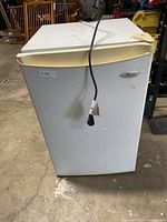 Front view of white Whirlpool mini fridge with cream-colored handle and power cord draped over the front.
