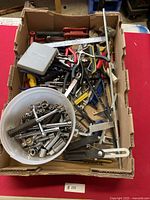 Overview photo showing a cardboard box containing various hand tools such as pliers, socket wrenches, rulers, Allen keys and small tools.