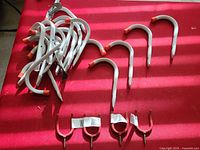 Photo of a cluster of white metal hooks with orange rubber tips and several red U-shaped metal hanger brackets on a red surface.