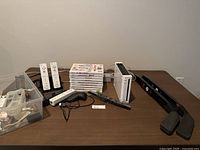 Full view of Nintendo Wii console with accessories on a table including 2 white Wii remotes, sensor bar, charging dock, and 10 Wii game cases.
