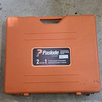 Closed orange hard plastic carrying case with handle, labeled Paslode FSC200 Flooring Stapler & Cleat Nailer