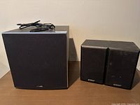 Front view of Polk Audio subwoofer and two Energy bookshelf speakers on a wooden surface showing front fabric grilles and logos.