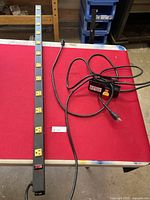 Long black power bar with 12 yellow outlets on red table.