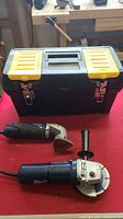 Two power tools (Master Craft power shaper sander and RONA mini grinder) and a black and yellow toolbox on red surface