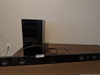 Samsung sound bar and subwoofer viewed from front on brown surface, showing speaker drivers and power cables.