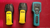 Front view of two Stanley stud finders and one EM4808 wood moisture detector on red background