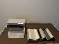Xyron 850 manual laminator with three extra laminating cartridge rolls laid out on table.