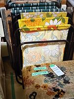 Assorted folding lawn chairs stacked, showing floral and striped webbing patterns on metal frames.