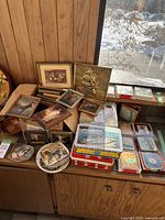 Overview photo showing assortment of coasters, picture frames, and decorative tins arranged on a wooden cabinet under window light