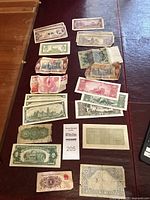 Assorted vintage banknotes arranged on a red surface showing various global origins and denominations, including visibly worn and folded notes.