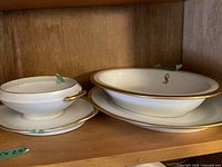 Two oval white serving dishes with gold trim stacked on a wooden shelf.
