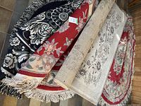Four rolled area rugs stacked showing top patterns and fringe on three pieces