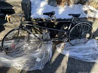 Full side view of gray tandem bicycle on plastic sheeting against stone wall