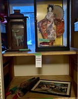 Porcelain deer figurine and Japanese Geisha doll in separate display cases, with textured art and umbrellas on lower shelf