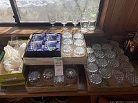 Overview of various glass and crystal glassware on a table, including boxed Edinburgh Crystal set, clear stemware, and pressed glass tumblers.