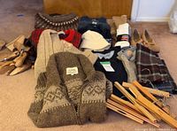 Overview of sweaters and cardigans in various colors and patterns, hats, scarves, and some shoes on carpet.