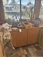 Various gardening pots, some containing plants, placed on wooden cabinet by window with view outside.