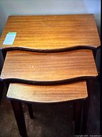 Top view of all three stacked wooden nesting tables showing wave detail on front edges and minor surface scratches