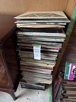 Full stack of vinyl records from the lot, various album covers visible, records leaning against a wooden surface