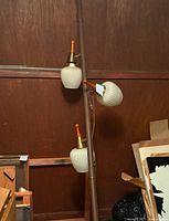 Full view of tall brown tension pole lamp with three white ribbed glass shades against wood wall