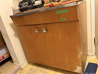 Front view of first wooden kitchen cabinet with red formica-style countertop, two doors, round metal knobs, showing wear and scuffs