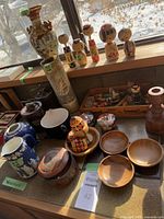 View of the Japanese Kokeshi dolls, tall decorative Japanese vase, and various wooden bowls and containers arranged on a table with natural light.
