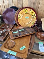 Multiple trays stacked including teak trays, one with three glass inserts, a painted floral tray, spoons, nutcrackers, and small wooden bowls