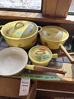 Front view of four yellow enameled cast iron cookware pieces by a window