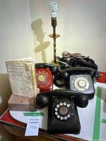 Photo showing three vintage rotary dial telephones in red and black, along with vintage Vancouver map and directory, and brass table lamp base visible