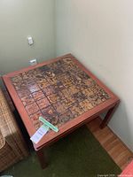 View of square wood framed table with tiled top showing abstract brown/yellow tiles.