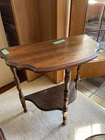Full view of vintage brown wood half moon side table showing curved top and bottom shelves with turned legs.