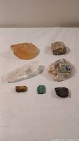 Seven assorted rocks and crystals arranged on a white surface showing size, color, and texture details