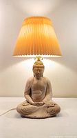 Front view of the ceramic Buddha lamp showing the pleated lampshade illuminated and Buddha statue base with detailed facial features and seated pose.