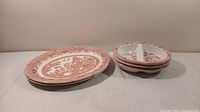 Pair of Churchill Red Willow porcelain serving platters stacked on the left and trio of bisected bowls stacked on the right, set on a table against a beige wall.