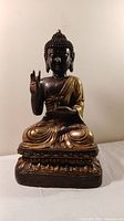 Front view of metal Buddha statue showing detailed face, hand gestures, and gold burnished robe.
