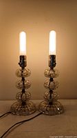 Pair of antique ribbed glass boudoir lamps illuminated with bulbs on, showing tiered ribbed glass design and metal sockets.