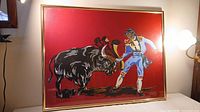 Full view of the Roberta Blair painting showing the matador and bull on red background in gold frame.
