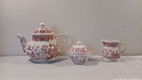 Full view of the trio: teapot, sugar bowl with lid, and creamer, all decorated with the red Willow pattern.