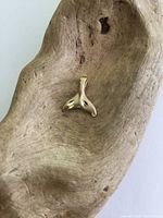 Front view of small yellow gold whale tail charm pendant placed on a textured wooden surface.