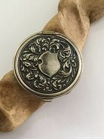 Top view of round silver plated change purse holder with detailed embossed shield and floral design on lid.