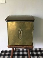 Front view of the antique brass firewood box with decorative motif on front and arched lid.
