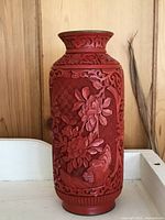 Front view showing detailed floral carvings and checkered textured background on red cinnabar lacquer vase